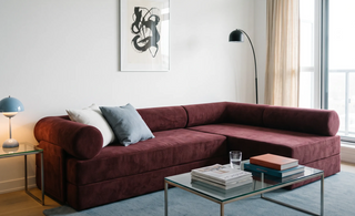 A modular sleeper sofa in a styled living room setting, featuring a center table, white and cow-print pillows, a black floor lamp, and a wall with art.