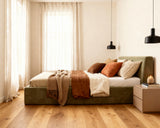 O2 Bed Cloud Frame in olive green, styled with warm-toned pillows, layered blankets, and textured throws in a cozy, modern bedroom with soft natural light.
