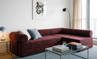 A modern modular sofa bed in a styled living room setting, featuring a table, white and cow-print pillows, a black floor lamp, and a wall with an art.