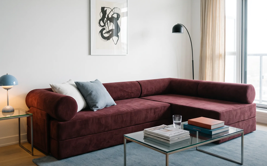 A modern modular sofa bed in a styled living room setting, featuring a table, white and cow-print pillows, a black floor lamp, and a wall with an art.
