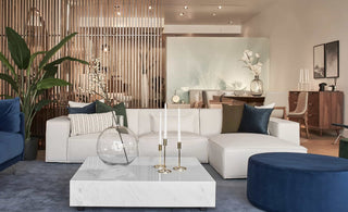 Modern white modular sofa in a stylish living room with navy blue accent chairs, a round ottoman, a marble coffee table, and contemporary decor.