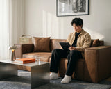 Man sitting on the M1 Sofa Sectional in a living room, with a coffee table in front of it.