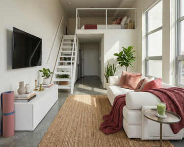 S8 Sleeper Sofa Bed in a compact studio-style space, positioned in front of a TV and media console, with a staircase in the background leading to a small bedroom.