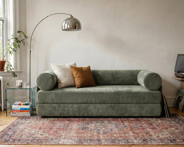 S8 Sleeper Sofa Bed in a living room, styled with two cushions, a rug, and a floor lamp beside it.