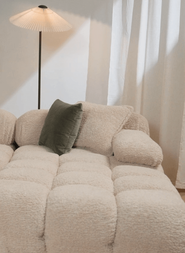 Beige sofa with a green pillow in a room with a lamp and curtains.